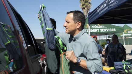 Assemblymember Rendon hands a backpack to a recipient through a car window