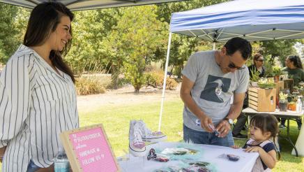 Assemblymember Rendon stands at a vendor's table showing his daughter something from the table