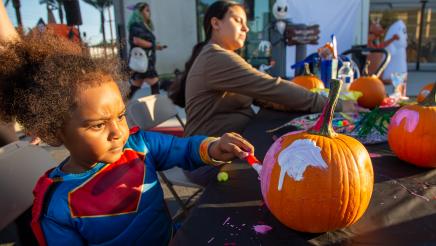 Child and adult seated at table, painting pumpkins