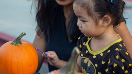 Child and parent at table, painting pumpkin