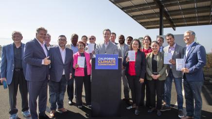 Governor Newsom signs legislation while surrounded by legislators.