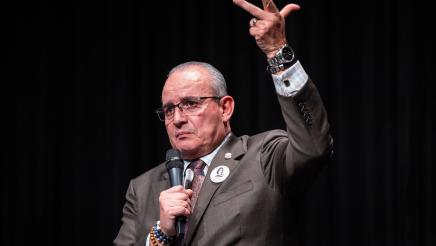 Guest speaker holding microphone, gesturing upward