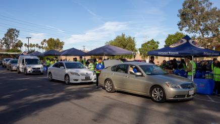 A line of cars alongside multiple tents, with volunteers distributing food